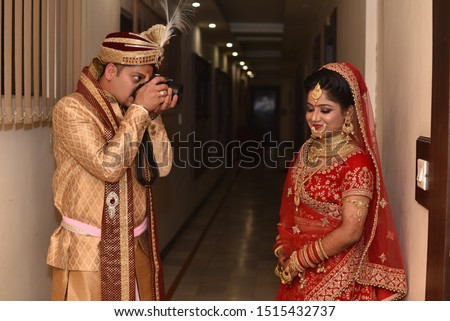 Young Indian wedding couple posing for photographs. Groom clicking picture of bride. The couple is  wearing traditional wedding dress which is designer lehenga and sherwani