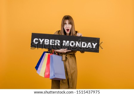 surprised excited girl in autumn coat and cyber monday sign and colorful shopping bags isolated over yellow