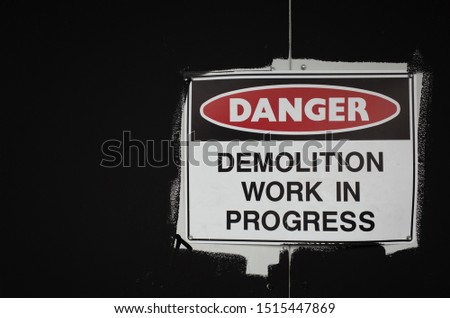 A sign of ' Danger, demolition work in progress ' on a black wall.