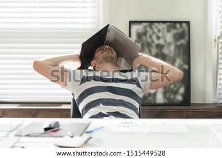 Tired business man sleeping at his desk covering his head with a laptop