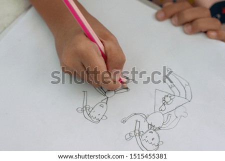 Hand of girl holding a pencil to practice drawing cartoons on white paper.