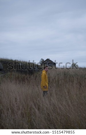 young man in a yellow raincoat in a field. happy young man wearing yellow raincoat standing in a wheat field. shows emotions. cheerful man in windy foggy mountain.