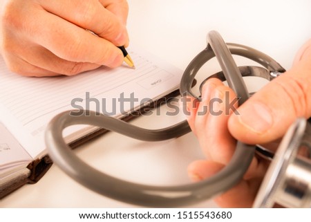 The doctor sits in an office at a white table, makes notes in a notebook, a stethoscope lies nearby, view from above.