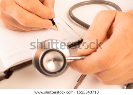 The doctor sits in an office at a white table, makes notes in a notebook, a stethoscope lies nearby, view from above.