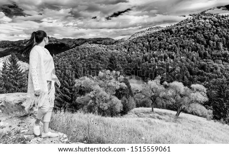 A girl on a rock admiring the Hornisgrinde mountains covered by fir forest and clouds, in the Black Forest, Germany. Travel destination.Black and white picture.