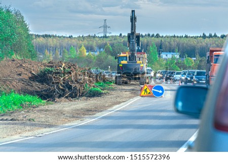 The excavator conducts road works. Travel is limited to one lane.