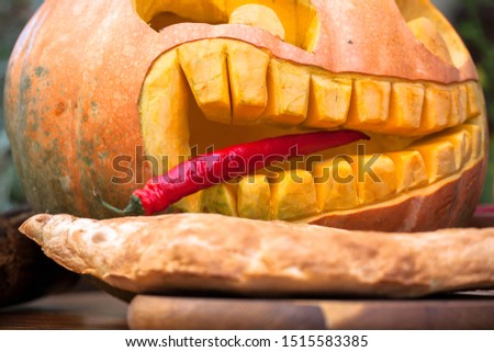 Hungry pumpkin with pepper. In mouth a pointy red pepper tongue sticks out between crooked tip teeth. Harvest of pumpkin.