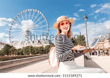 Happy Asian self-employed girl or student learning a language over the Internet sitting with a laptop in the amusement Park with Ferris wheel at the background