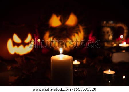 Close up candle with two unfocused carved pumpkins with scary faces jack o lantern on background in the dark. Halloween concept.