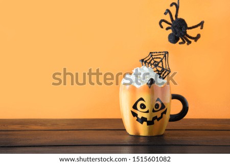 Cup of coffee latte garnish spider web and coming black spider. Halloween holiday treat on wooden table.