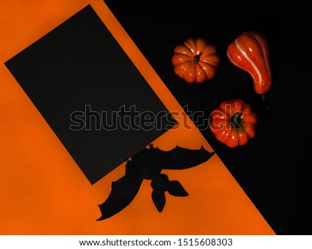 Halloween holiday concept. A bat, a blank sheet of black paper on an orange background, orange pumpkins on a black background.