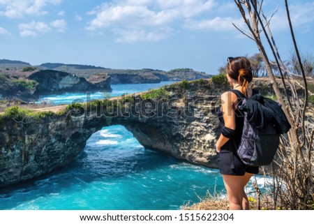 Travel people with backpack and in shorts on the ocean, cliffs and tropical beach background. Angel's Billabong beach, Nusa Penida, Indonesia. 