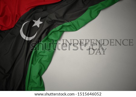 waving colorful national flag of libya on a gray background with text independence day. concept