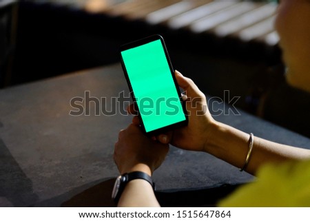 Over the shoulder view of young man looking at green screen smartphone at night