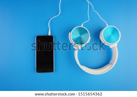 blue white color headphone placed next to handphone on a blue background