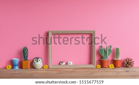 Beautiful  cactus,blank  wooden  picture  frame,simulated  owls  and  pine  cone  on  wood  table  with  pink  background