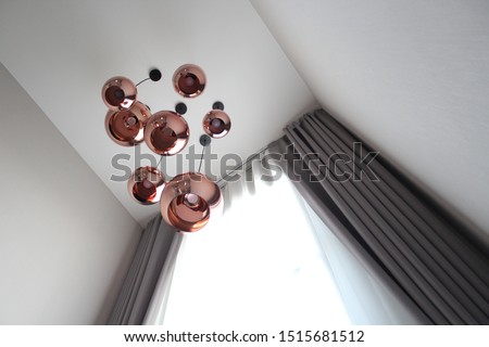 The beautiful lamps with copper colour hang on the high ceiling with grey curtains with sheer curtains at the stair way. Interior design with modern style , earth tone, living room, contemporary. Royalty-Free Stock Photo #1515681512