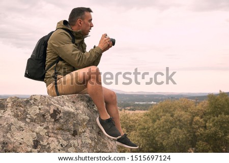 A nature photographer shooting and sitting down on a rock during sunset.
