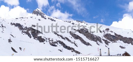 Panoramic view of a snowy mountain with visible rocky parts under the blue sky