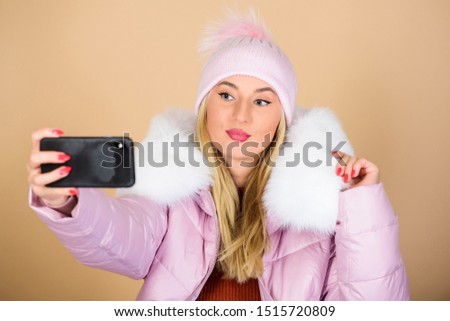 woman in beanie hat. happy winter holidays. web blogger. girl in puffed coat make selfie. faux fur fashion. warm winter clothing. phone selfie. flu and cold season. Leather bag fashion.