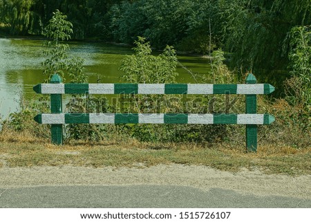 wooden striped barrier by an asphalt road on the shore of a forest lake