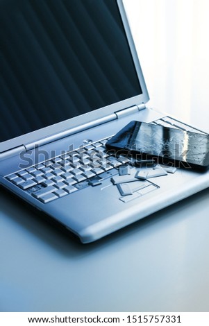 A silver laptop with a broken keyboard and a tablet with a cracked display. A close-up 
picture of part of broken laptop and cracked screen on a tablet.