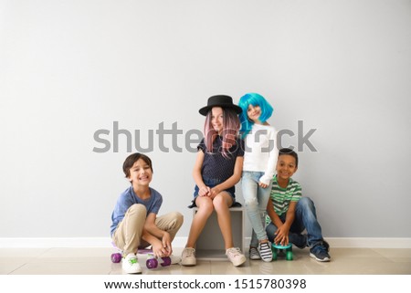 Stylish little children with skateboards near light wall