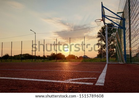 Outdoors mini football and basketball court with ball gate and basket surrounded with high protective fence.