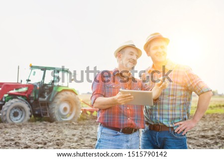 Farmers discussing over digital tablet in field with yellow lens flare in background