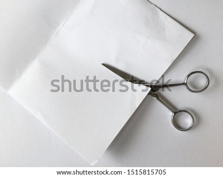 The scissors are cutting the white drawing paper