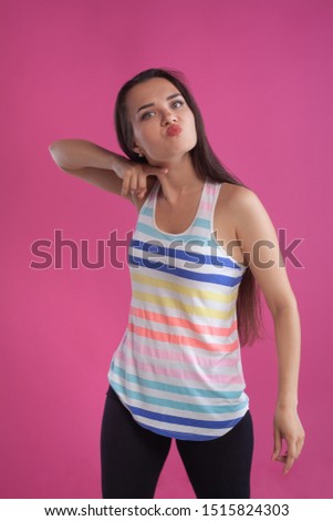 Brunette woman with long hair, dressed in colorful striped shirt, posing against pink studio background. Sincere emotions. Close-up.
