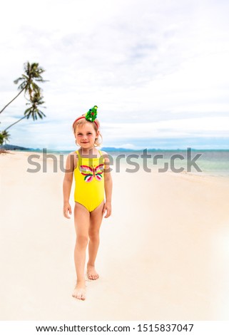 Little girl in the rim in the form of Christmas trees and yellow swimsuit is standing on the beach