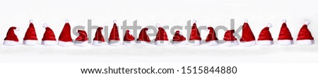 many little red santa claus hats in a row with snow and flakes for the christmas december time on a white background