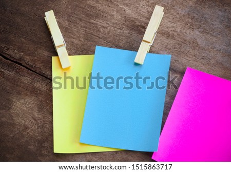 blank paper note color yellow blue pink with paper clip on wood background.