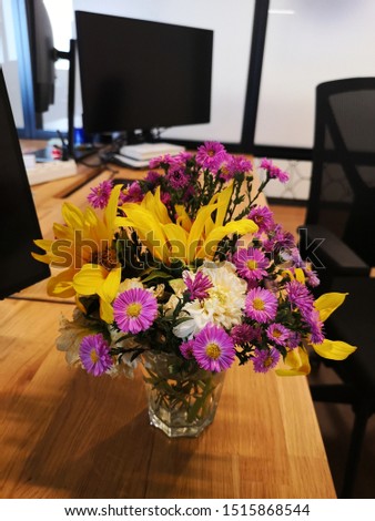 Bouquet of autumnal pink white and yellow flowers in a white glass vase, on an office desk.