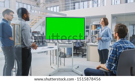 In the In Industrial Design Facility Team of Engineers and Technicians have a Meeting, Female Specialist Leads Briefing, Talks and Use Digital Interactive Whiteboard with Green Mock-up Screen