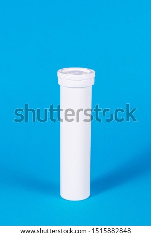 Round white matte aluminum tube with cap for effervescent or carbon tablets, pills, vitamins. Side view. New sealed vertical tube for storing medicine, isolate on a blue background. copy space