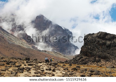 Heavily laden "Kili-fighters" trek towards the infamous Lava Tower of Mount Kilimanjaro, Tanzania, with the mist-clad peak in the background