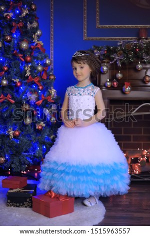 young girl with a diadem in white with a blue Christmas dress by the Christmas tree