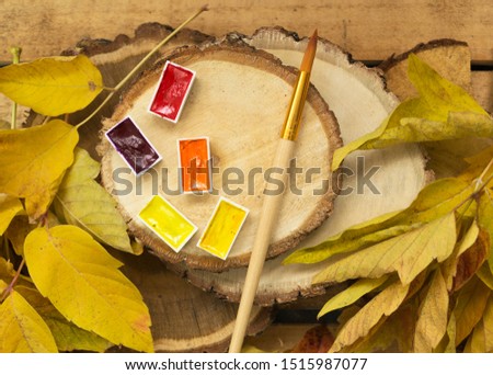 Autumn background with yellow leaves of trees, with yellow, red, orange watercolor paint and with an art brush lie on wooden log cabins. Bright autumn concept.