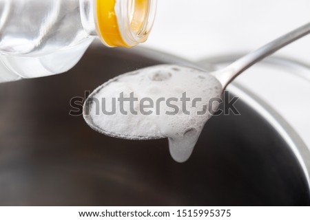 Baking soda slaked with vinegar in a spoon over a metal dish. Reaction between soda and vinegar with active foam. Royalty-Free Stock Photo #1515995375