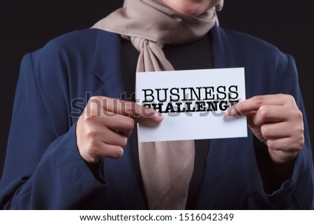 Businesswoman holding a white card with the word "Business Challenge" written on it.isolated on grey background.