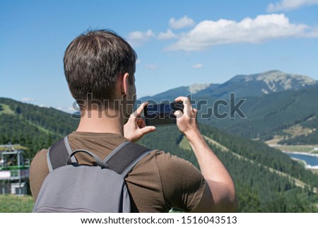 A tourist takes pictures on a smartphone by the mountain. A traveler takes videos and photos of nature.