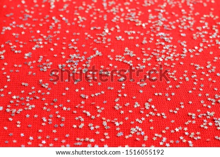 Top view with christmas silver stars. Silver stars confetti on a red knitted background. New year, winter, christmas background.