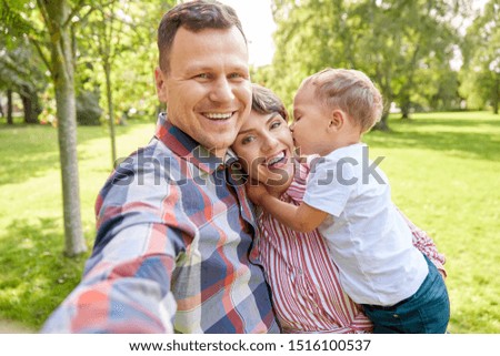 family, leisure and people concept - happy mother, father and little son taking selfie at summer park
