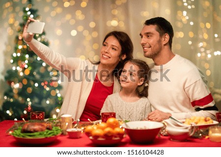 holidays, family and celebration concept - happy mother, father and little daughter having christmas dinner and taking selfie picture by smartphone at home