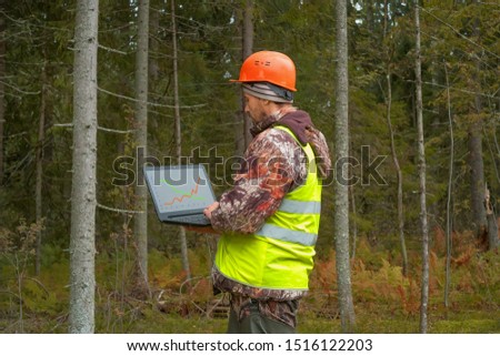 The forester analyzes the condition of the forest using a computer. On the computer screen graph. Forestry and forest worker.