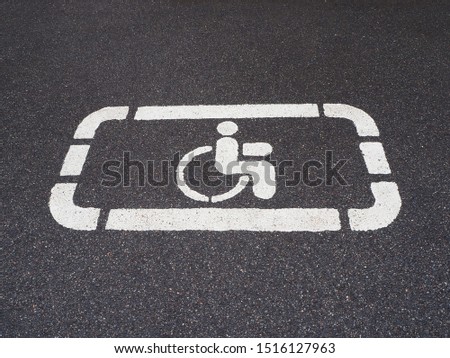 White handicapped symbol of wheelchair painted on asphalt on a parking lot, sign of parking space for disabled visitors. Free parking for disabled people's car. Empty disabled parking space.