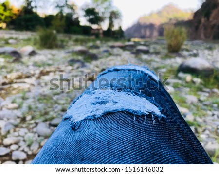 Leg in jeans taking picture of river side pebble and natural landscape.