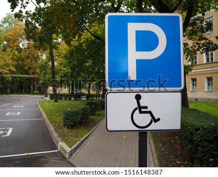 Blue road sign for disabled parking with autumn trees on background. Empty disabled parking space. Black handicapped symbol of wheelchair on a parking lot, sign of parking space for disabled visitors.